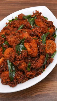 a white bowl filled with meat and greens on top of a wooden table next to a fork