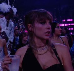 the woman is holding a drink in front of other people at a convention or show