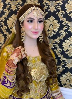 a woman wearing a yellow and purple outfit with gold jewelry on her head, in front of a wall