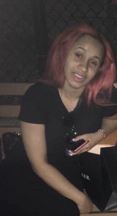 a woman with pink hair sitting on a bench in front of a laptop and holding a cell phone