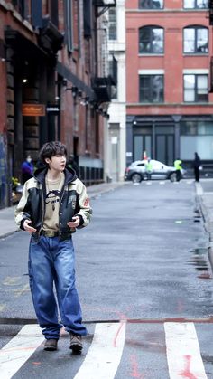 a young boy standing in the middle of a cross walk on a city street with buildings behind him