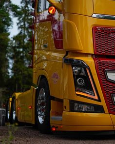 the front end of a yellow semi truck parked in a lot with trees behind it