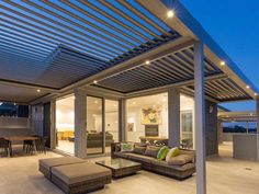 an outdoor living area with couches, tables and chairs under a pergolated roof