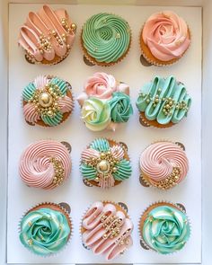 twelve cupcakes in a box decorated with pastel and gold icing designs