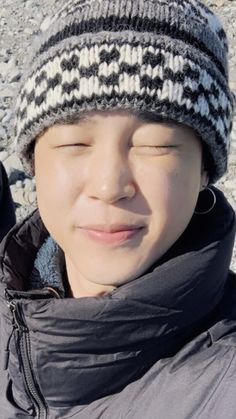 a young boy wearing a hat and jacket with his eyes closed while laying on the ground