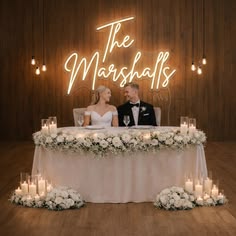 a bride and groom sitting at a table with candles in front of the sign that says the marshalls
