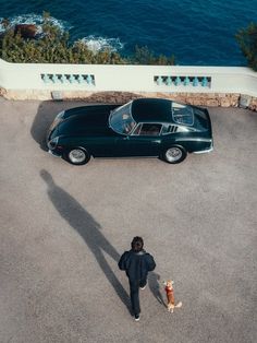 a man walking his dog in front of an old black sports car on the road