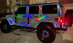 a white jeep with multicolored lights parked in front of a brick building at night