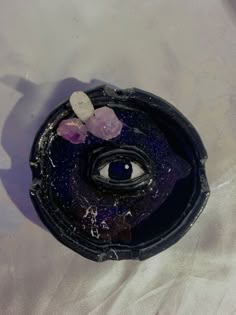 a black object with purple and white stones on it's surface, in the shape of an eye