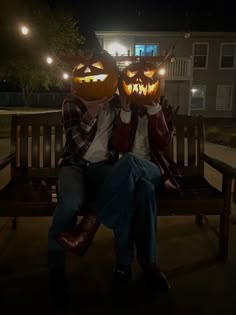 two people sitting on a bench with pumpkins carved into their faces at night time