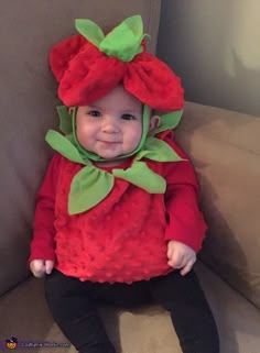 a baby in a red strawberry costume sitting on a couch