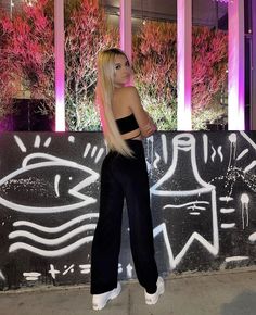 a woman standing next to a wall with graffiti on it