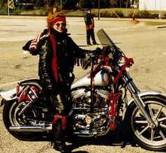 a woman standing next to a motorcycle in a parking lot with other people behind her