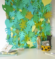 there is a paper cut out of leaves on the wall next to a vase and some books
