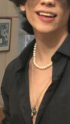 a woman with short hair wearing a black shirt and pearl necklace