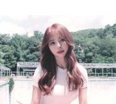 a woman with long hair standing in front of a lake