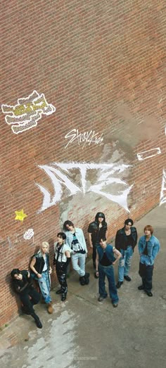 a group of people standing in front of a brick wall with graffiti on the side