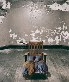 a bed sitting in the middle of a wooden floor next to a wall with peeling paint