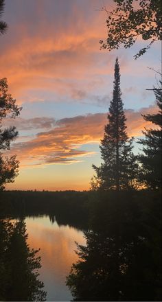the sun is setting over a lake with some trees around it and clouds in the sky