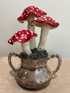 three red mushrooms sitting on top of a silver pot