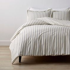 a bed with white and blue striped sheets on top of it, next to a wooden floor