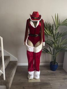 a santa suit and hat on display in front of a stair case next to a potted plant
