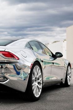 a silver sports car parked in a parking lot next to a white building and cloudy sky