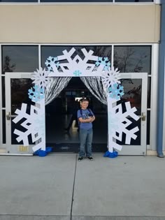 a young boy standing in front of an entrance decorated with snowflakes and ribbons