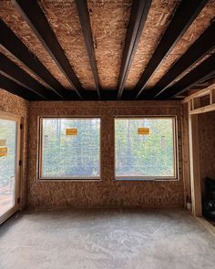 an empty room with two windows in the wall and some wood framing on the ceiling