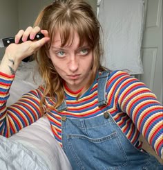 a woman in overalls holding up a remote control to her head and looking at the camera