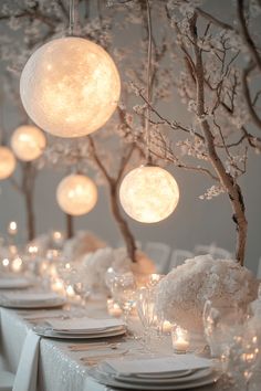 the table is set with white plates and place settings, lit by hanging lights above them