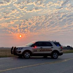 an suv is parked on the side of the road as the sun sets in the distance