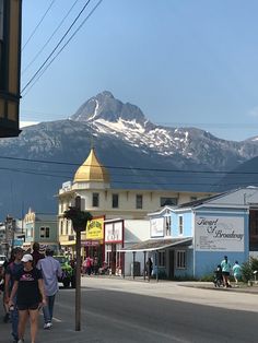 people are walking down the street in front of some buildings with snow capped mountains behind them