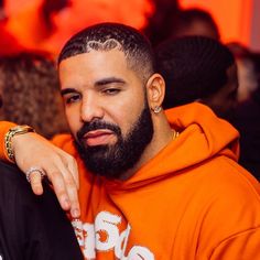 a man with a beard wearing an orange hoodie sitting in front of a crowd