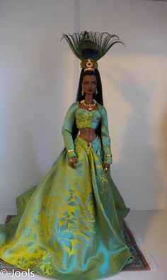 a barbie doll dressed in a green and gold gown with feathers on her head wearing a tiara