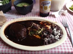 a white plate topped with meat covered in gravy next to a bottle of beer