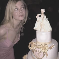 a woman standing next to a white and pink cake with gold decorations on it's sides