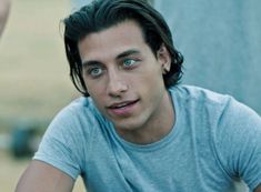 a man with long hair and blue eyes sitting on a bench looking at the camera