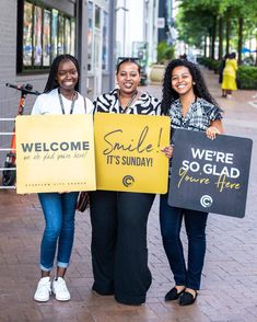 three women holding up signs that say welcome to the sundae and smile it's sunday