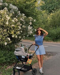 a woman walking with a stroller on the side of a road next to flowers