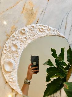 a person taking a selfie in front of a round mirror with plants on it
