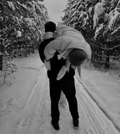 a man carrying a baby on his back while walking through the snow in front of trees