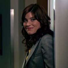 a woman standing in front of a door wearing a suit and smiling at the camera