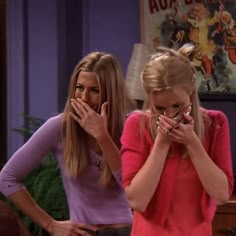 two young women standing next to each other with their hands covering their mouths in front of them