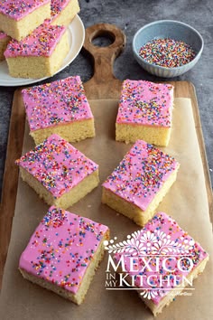 several pieces of cake with pink frosting and sprinkles on a cutting board