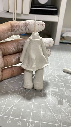 a hand holding a small white doll on top of a table next to a knife
