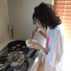 a woman standing in front of a stove cooking food on top of a frying pan
