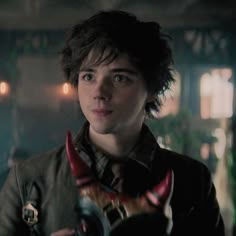 a young man with horns on his neck holding something in one hand and looking at the camera