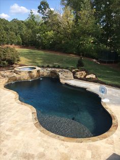 an outdoor swimming pool surrounded by stone walls and landscaping area with trees in the background