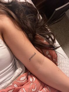 a woman laying on top of a bed with a tattoo on her arm and shoulder